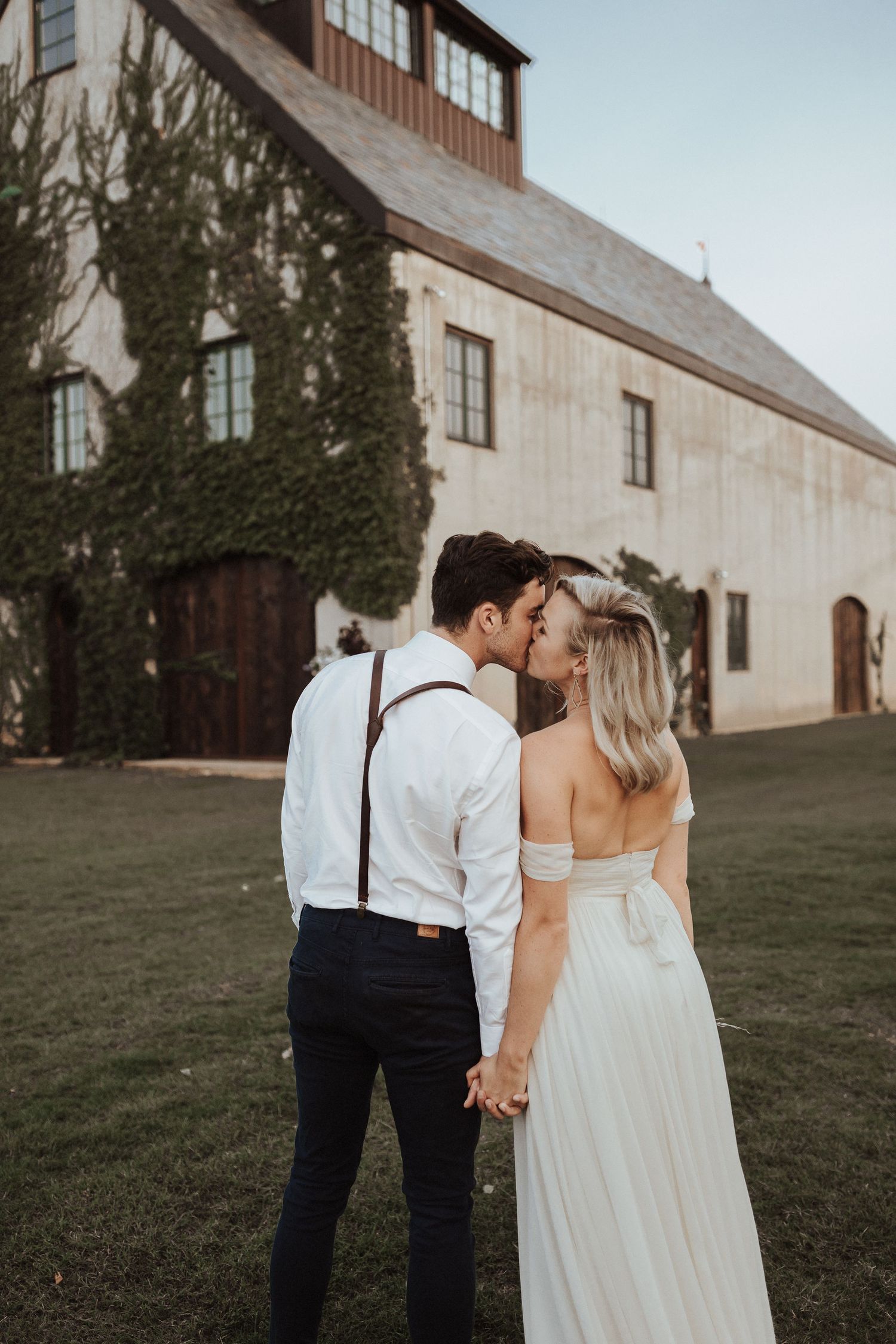 A couple shares a romantic moment outside a rustic barn with ivy-covered walls during golden hour.