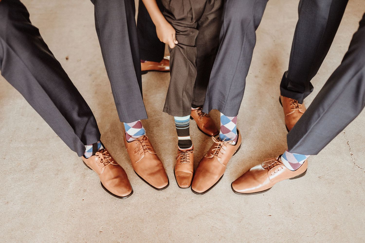 A group of people wearing coordinated brown leather dress shoes and gray pants stand together in a circle.
