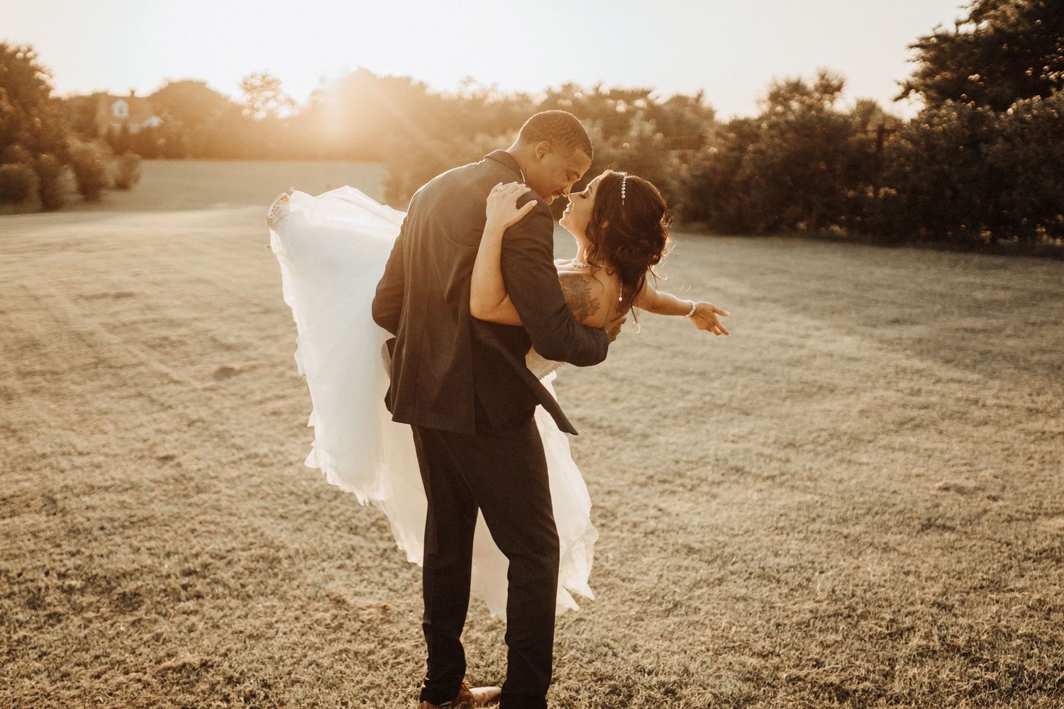 A newlywed couple embraces during golden hour in a sun-drenched meadow at sunset.