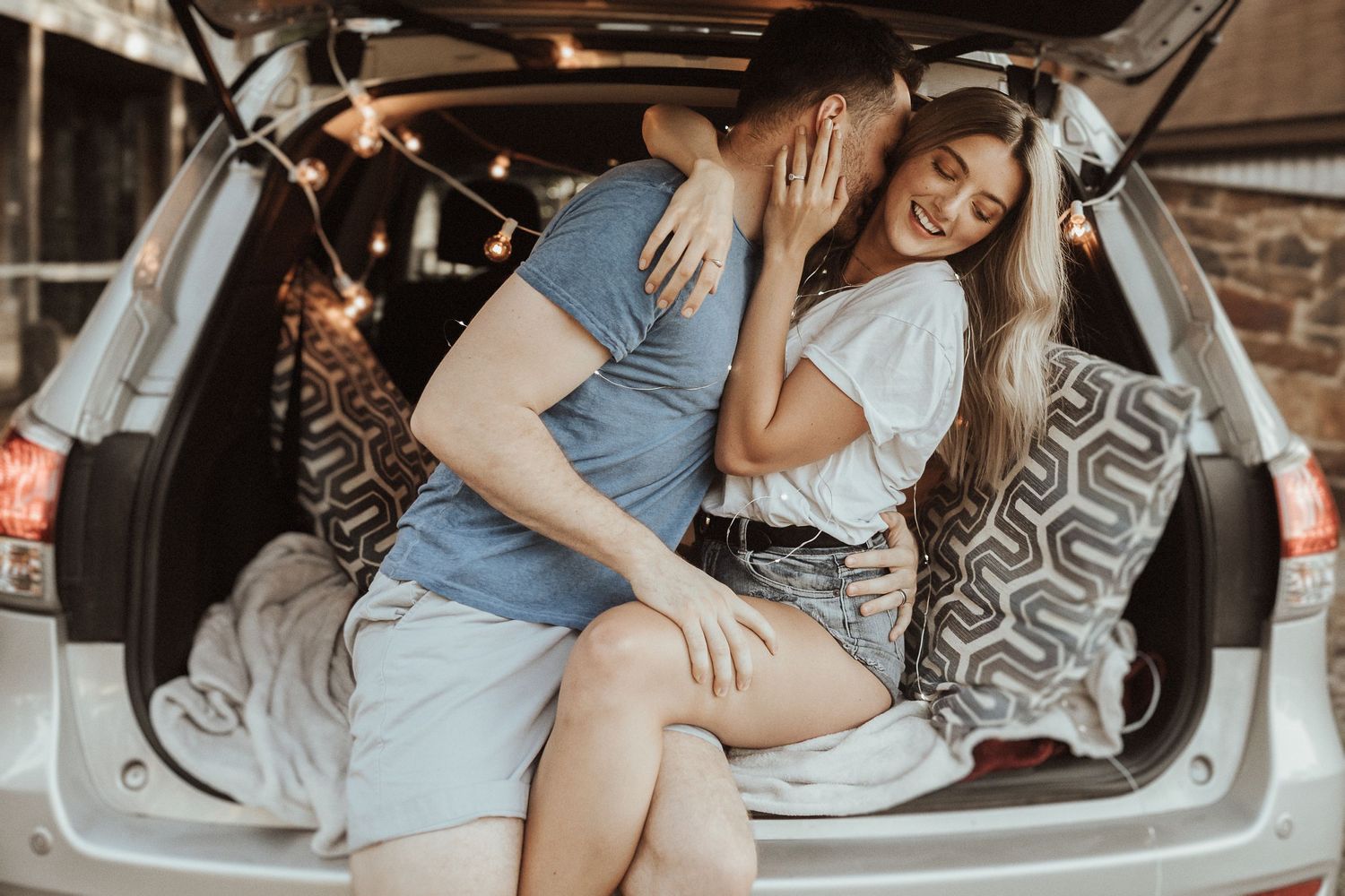 Couple enjoying a romantic moment in the back of their car with decorative pillows and natural lighting.