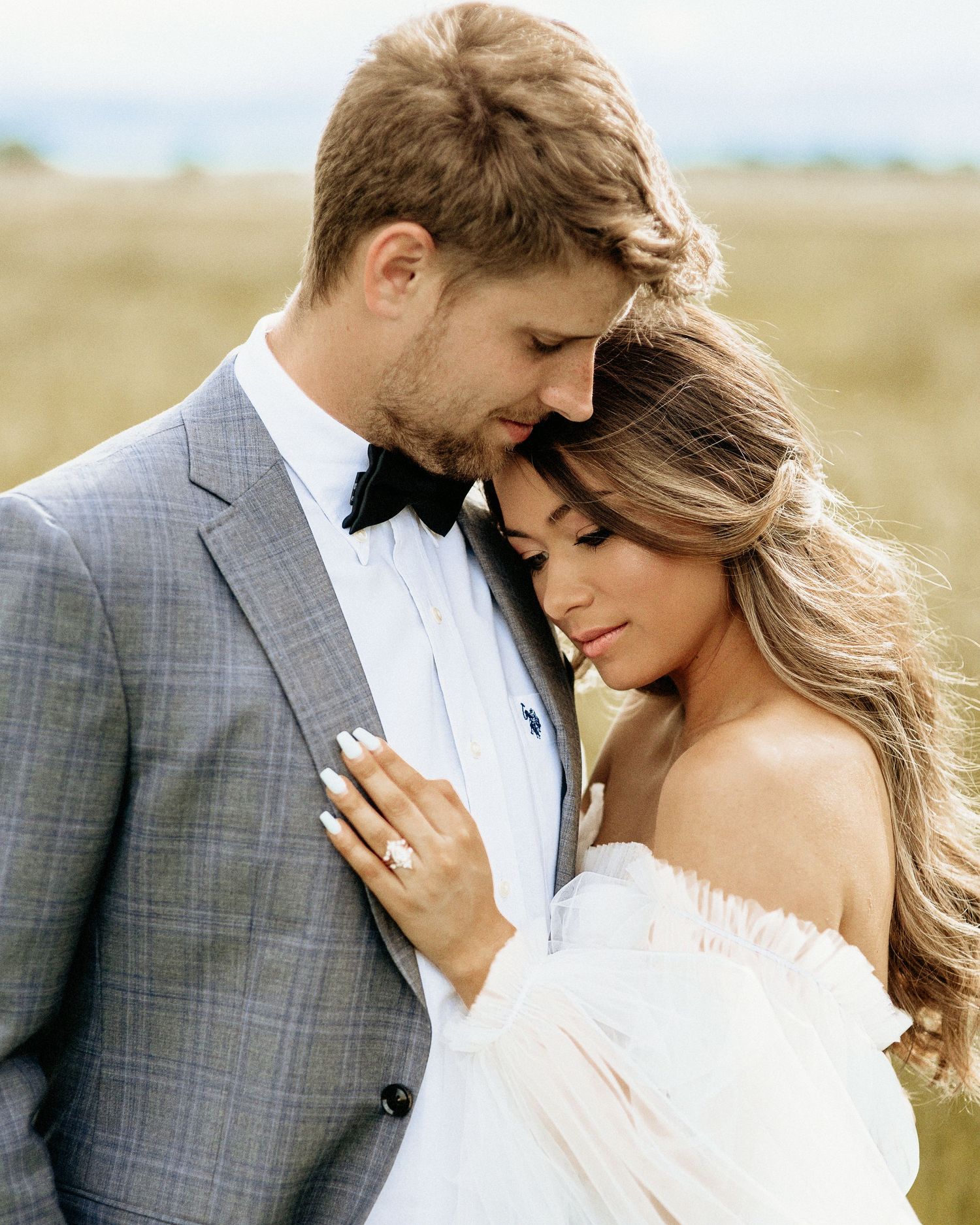 A romantic wedding portrait showing a couple embracing in elegant attire against a soft natural background.