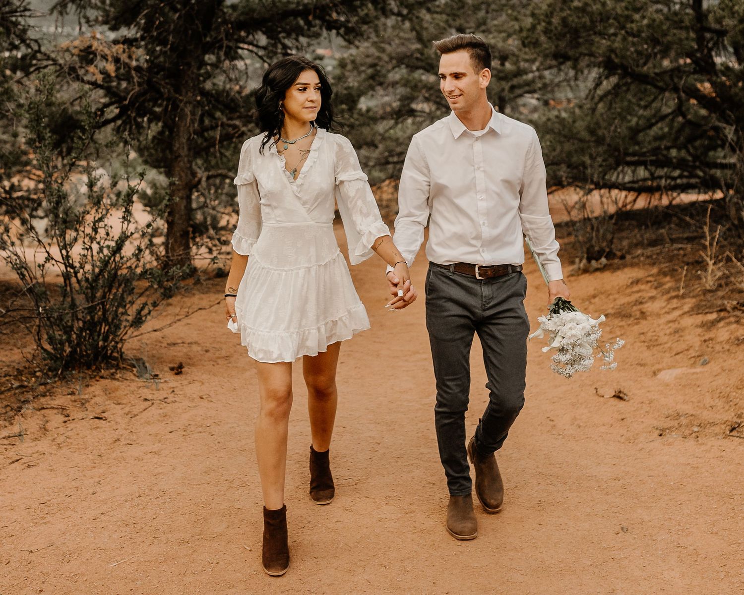 A couple walking hand in hand on a desert trail wearing white outfits in warm golden light.
