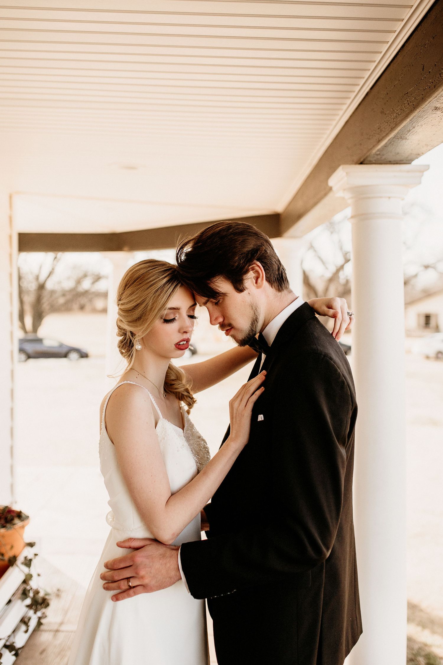 A romantic moment captured between newlyweds embracing on a covered porch at their wedding.