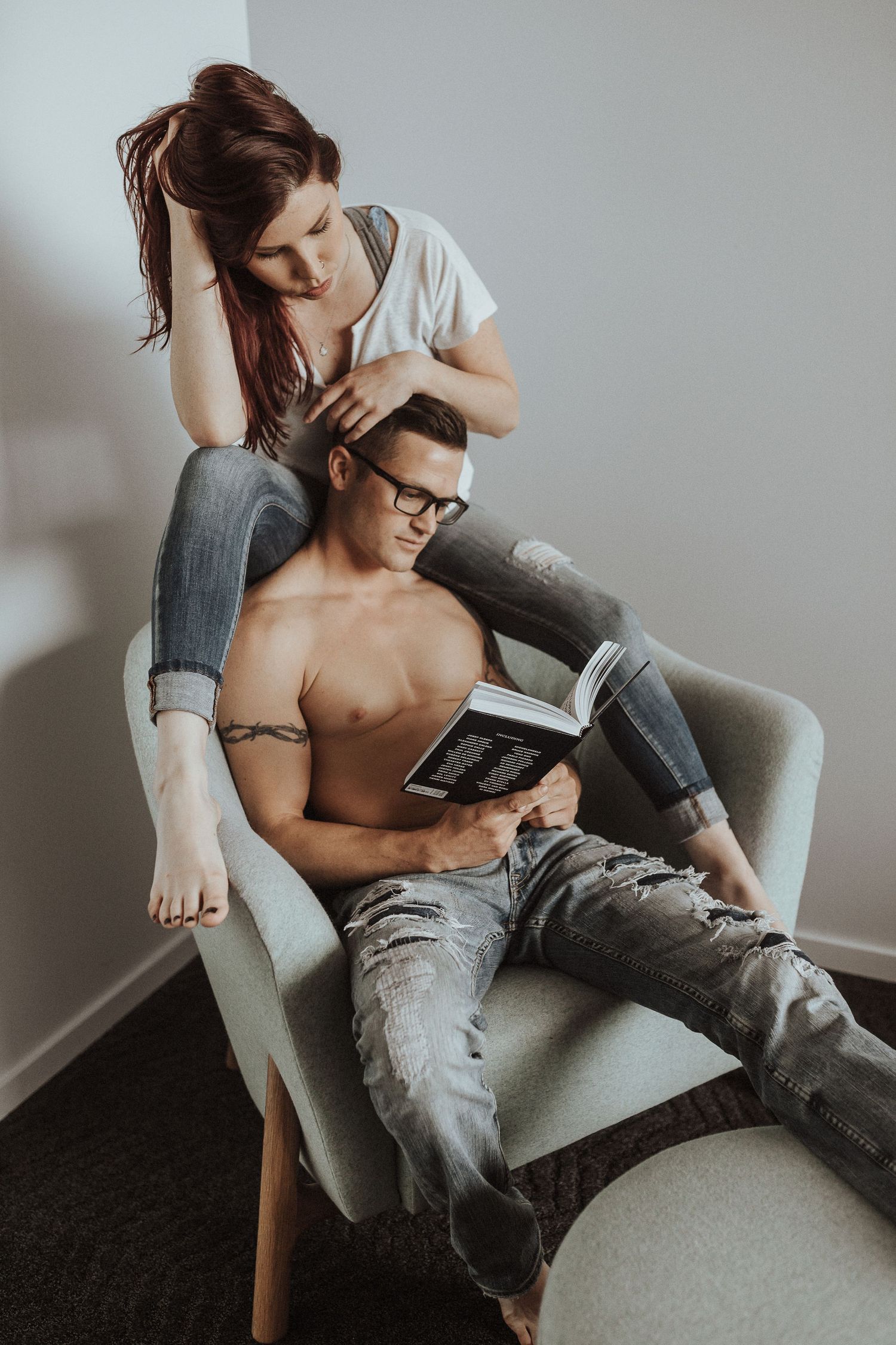 Intimate lifestyle photo of a couple reading together in a cozy armchair, with soft natural lighting and muted tones.