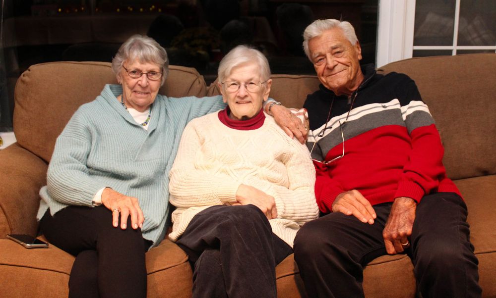 Three seniors sitting together on a brown couch in casual clothing.