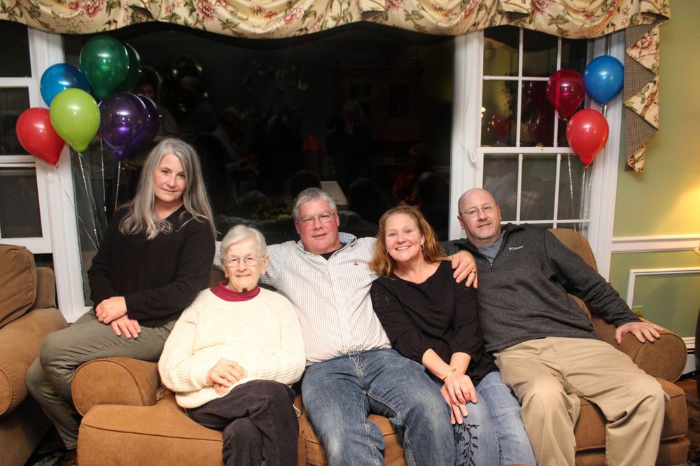 Family gathering on a couch with colorful balloons decorating the window behind them.