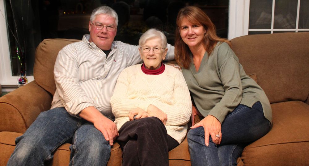 Three people seated on a comfortable brown couch in a home setting.