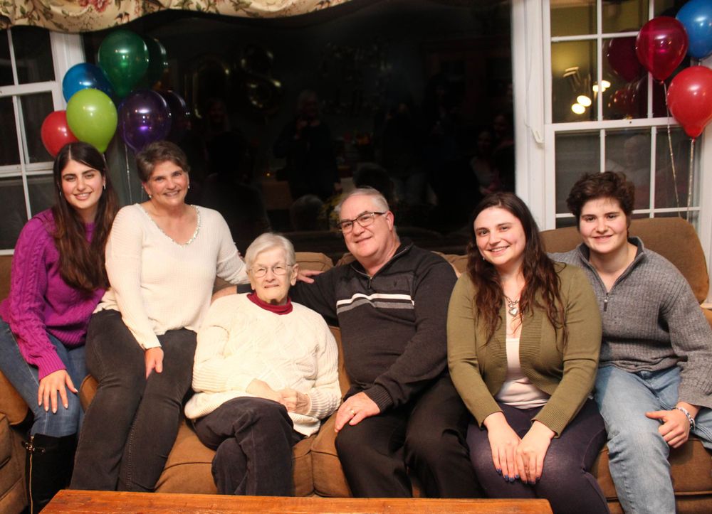 Family portrait on a couch with colorful balloons decorating the background.