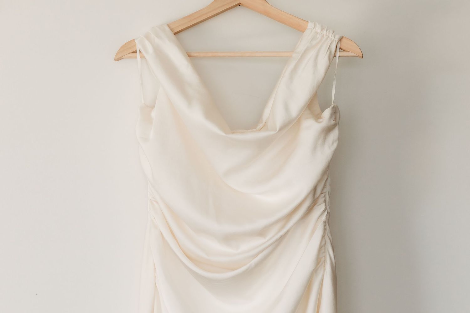 White wedding dress hanging on wooden hanger against light gray wall.