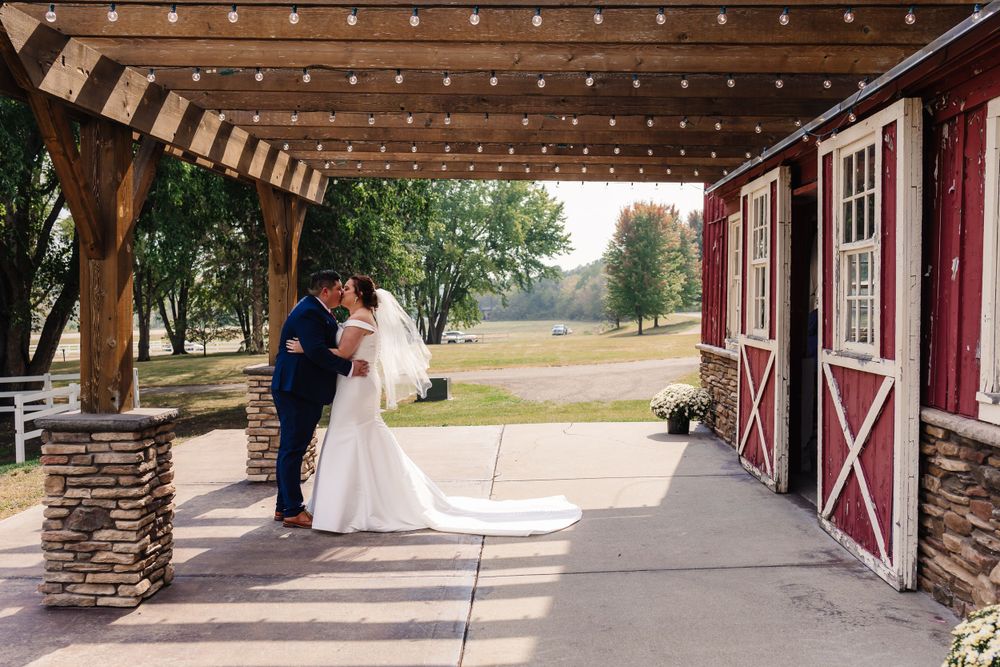 A couple shares a romantic moment under string lights outside a red barn wedding venue.