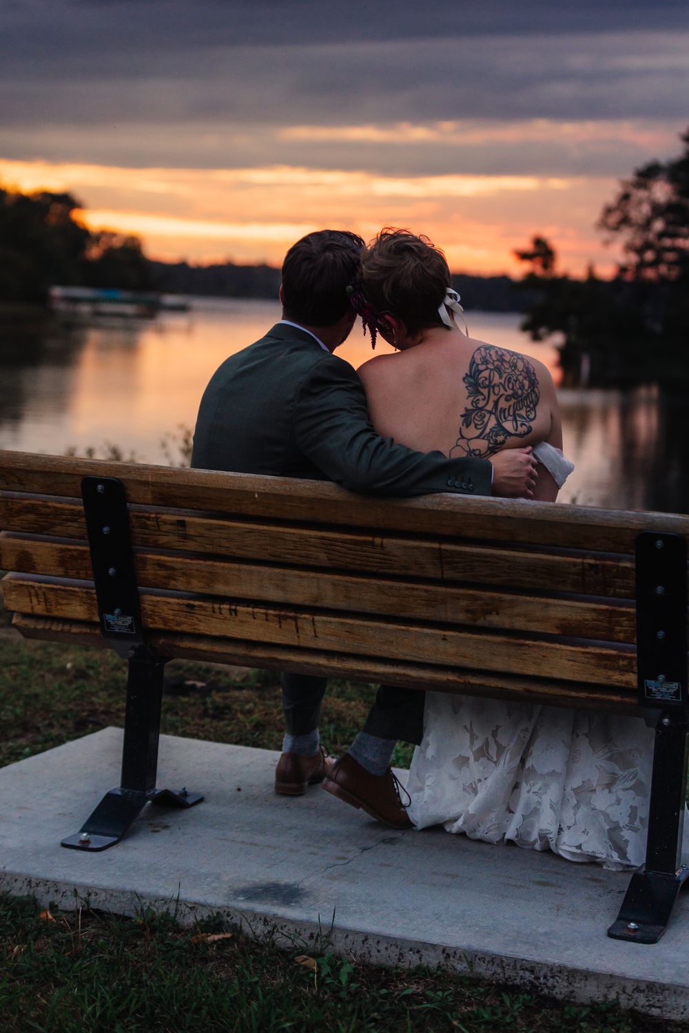 Couple sits together on wooden bench during sunset by the water.