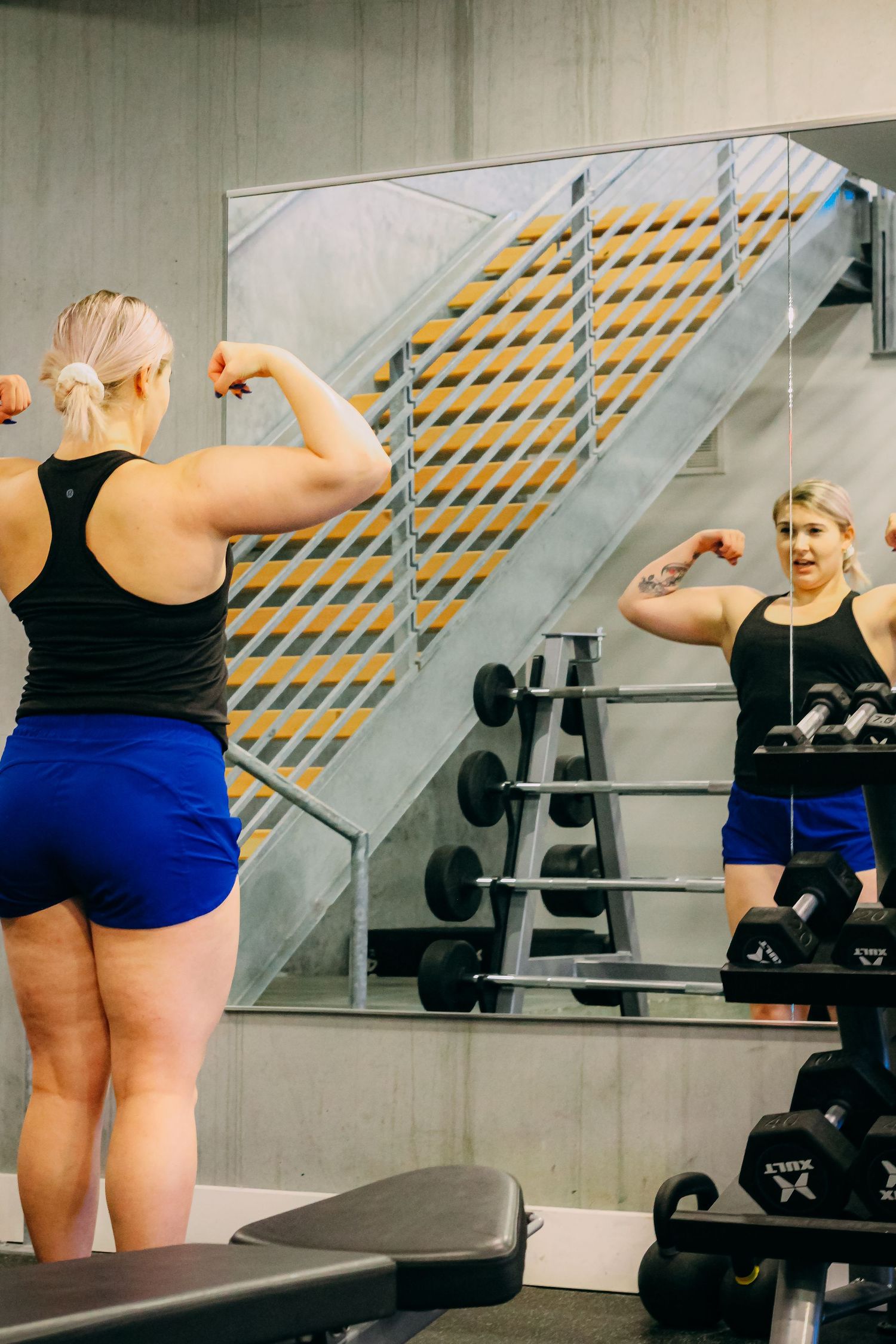 Fitness enthusiast checking form in gym mirror during workout session.