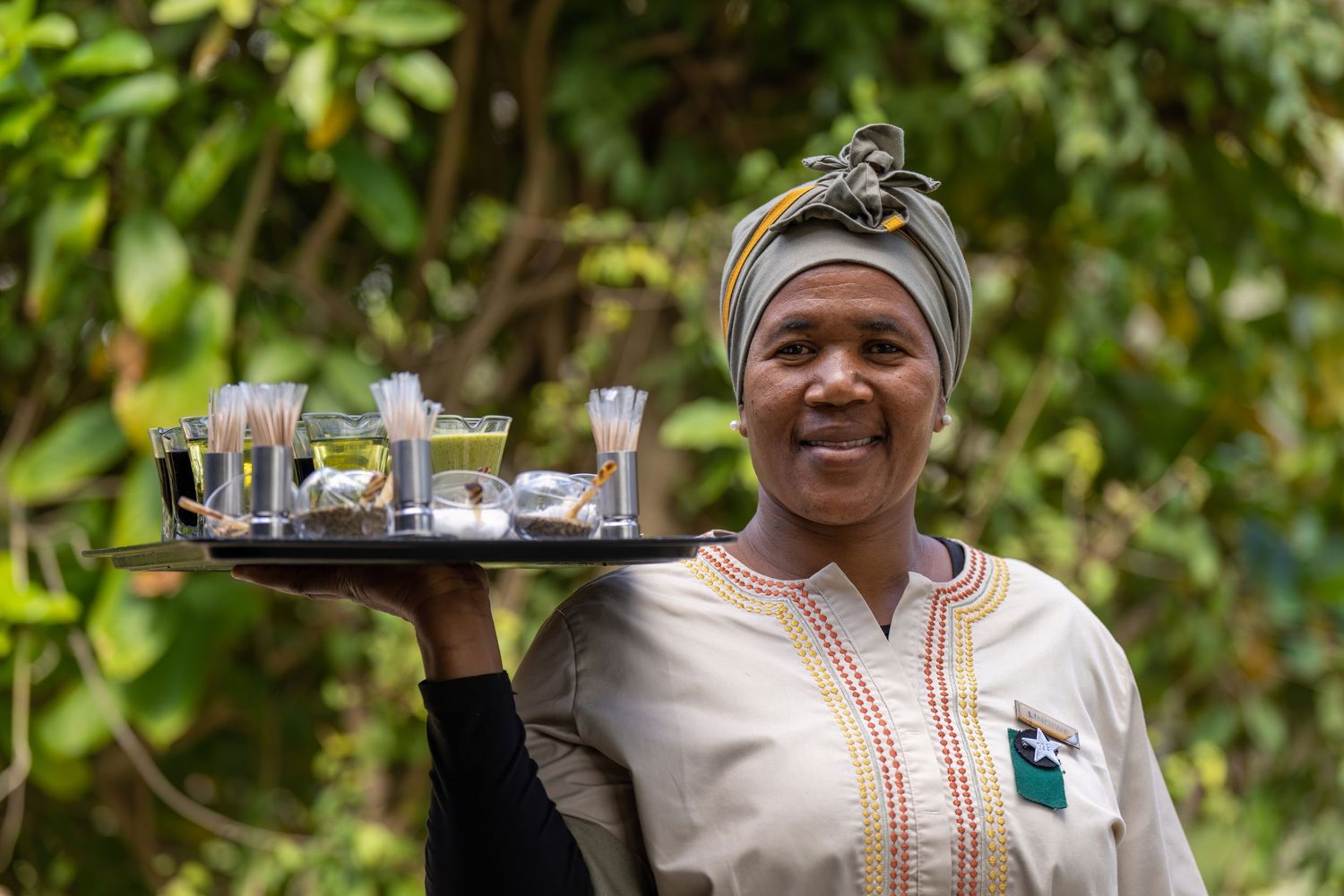 Staff carrying refreshment trays through lush garden setting at luxury safari lodge.