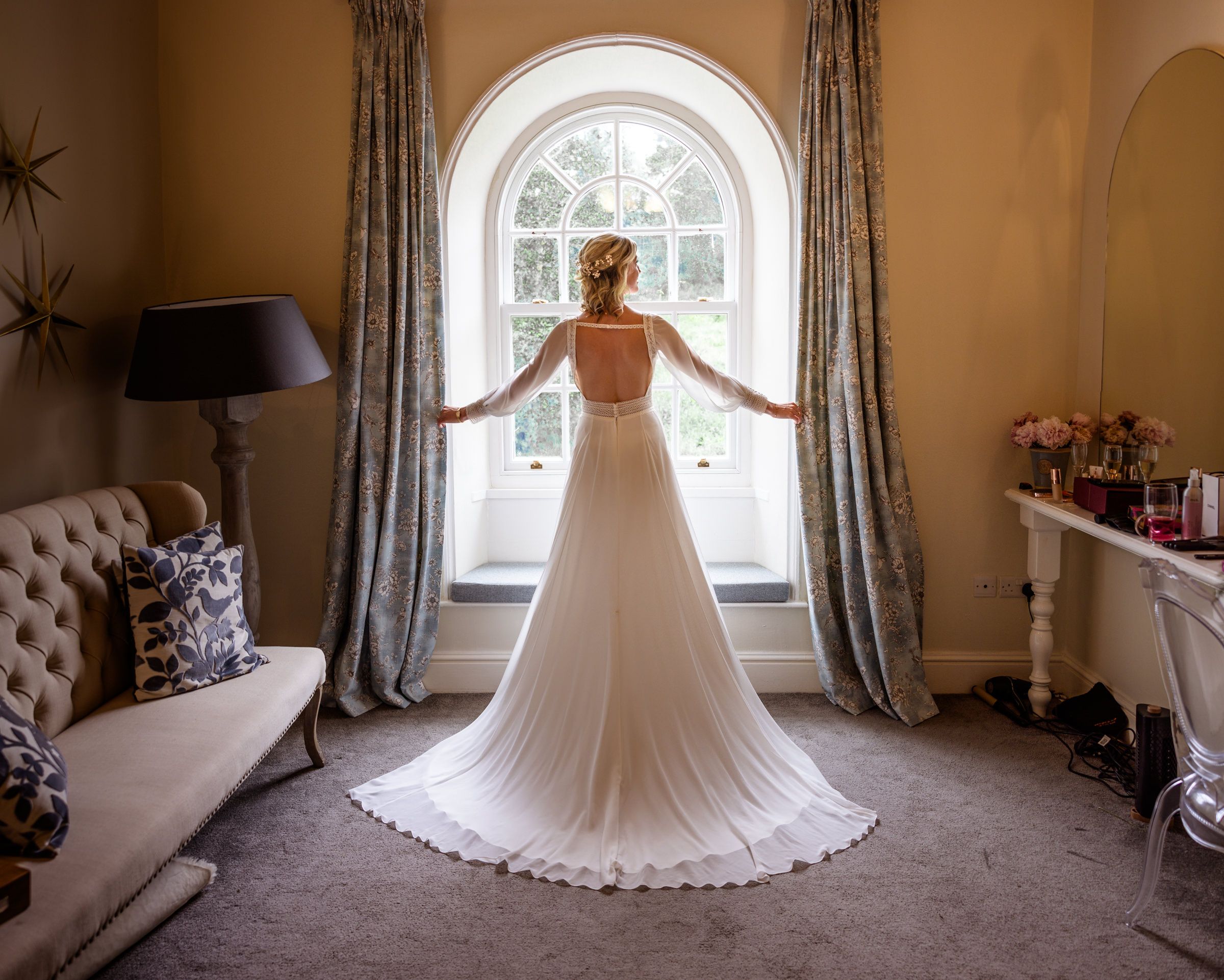 Elegant bridal gown silhouetted against an arched window in a luxurious interior setting.