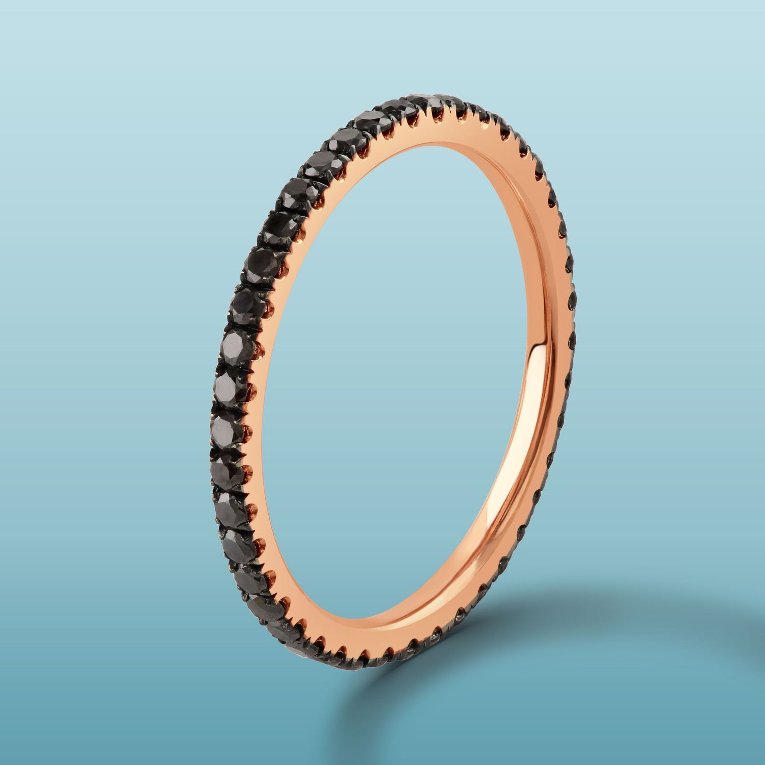Delicate rose gold eternity ring with black diamonds against blue gradient background.