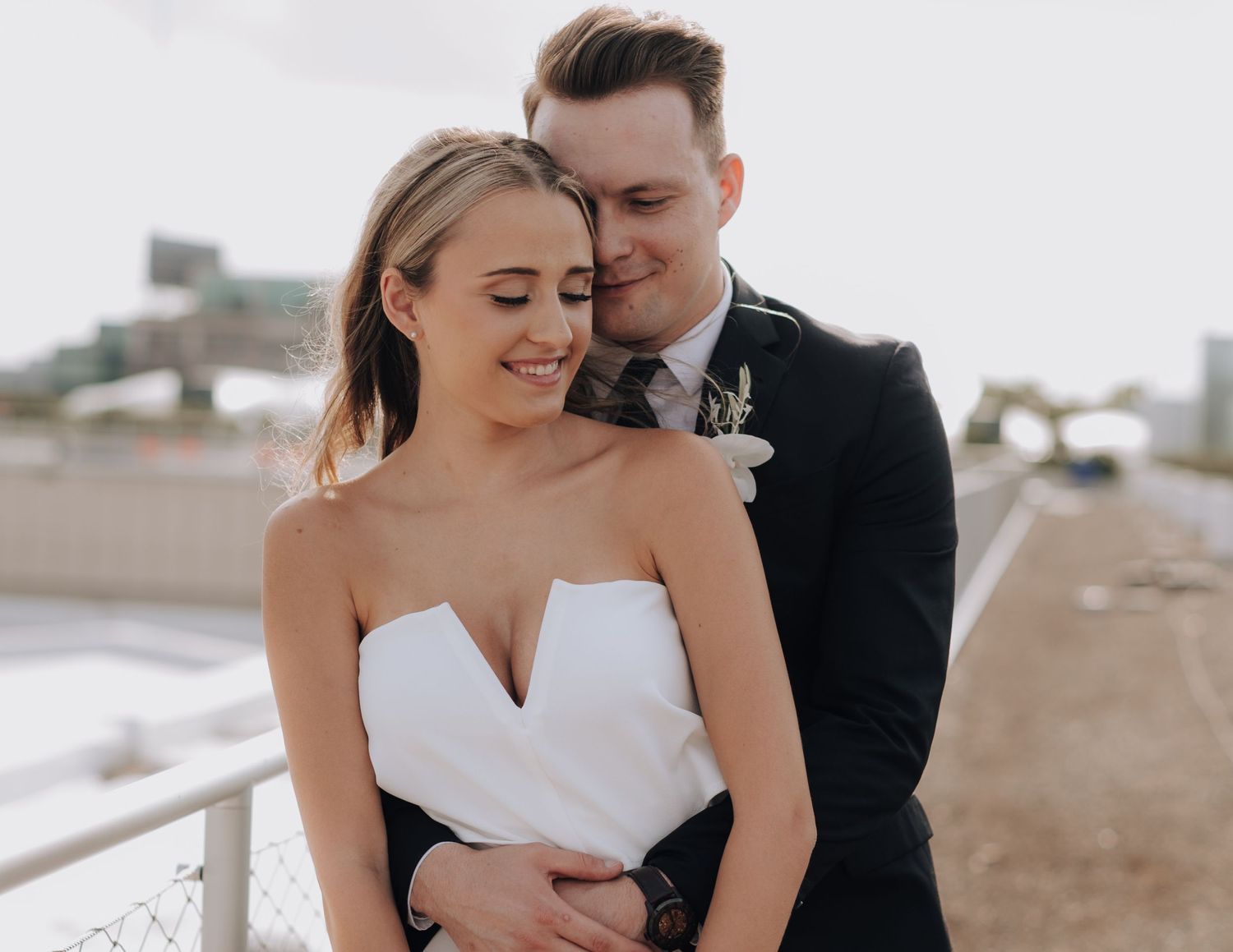 Intimate moment between newlyweds in formal attire against urban backdrop.