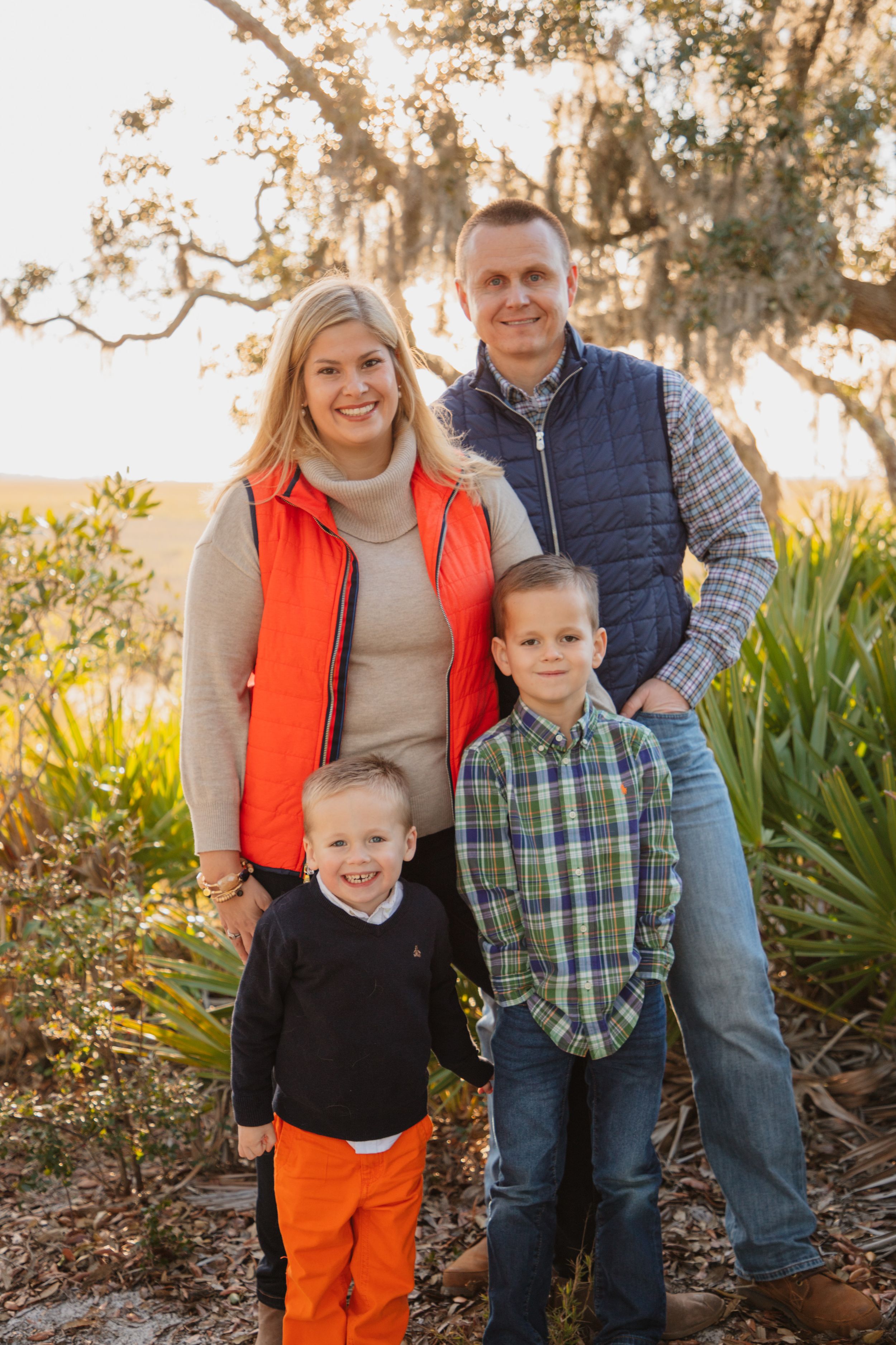 Happy family of four poses outdoors against a backdrop of Spanish moss trees at sunset.
