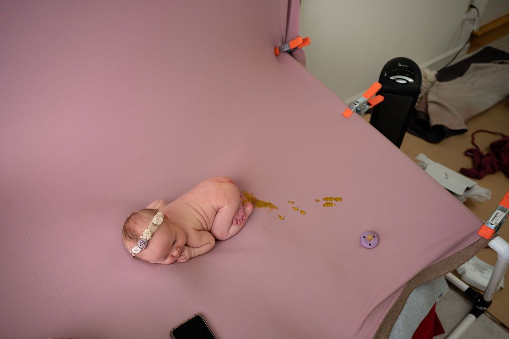 A sleeping newborn baby on a pink backdrop with a glitter stain.