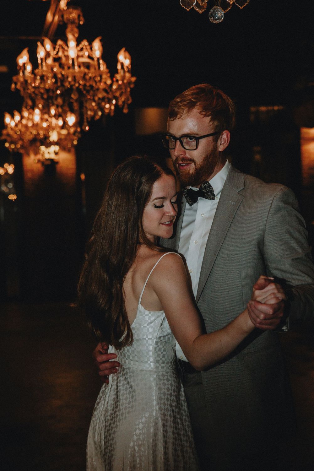 A couple dances together lit by chandeliers