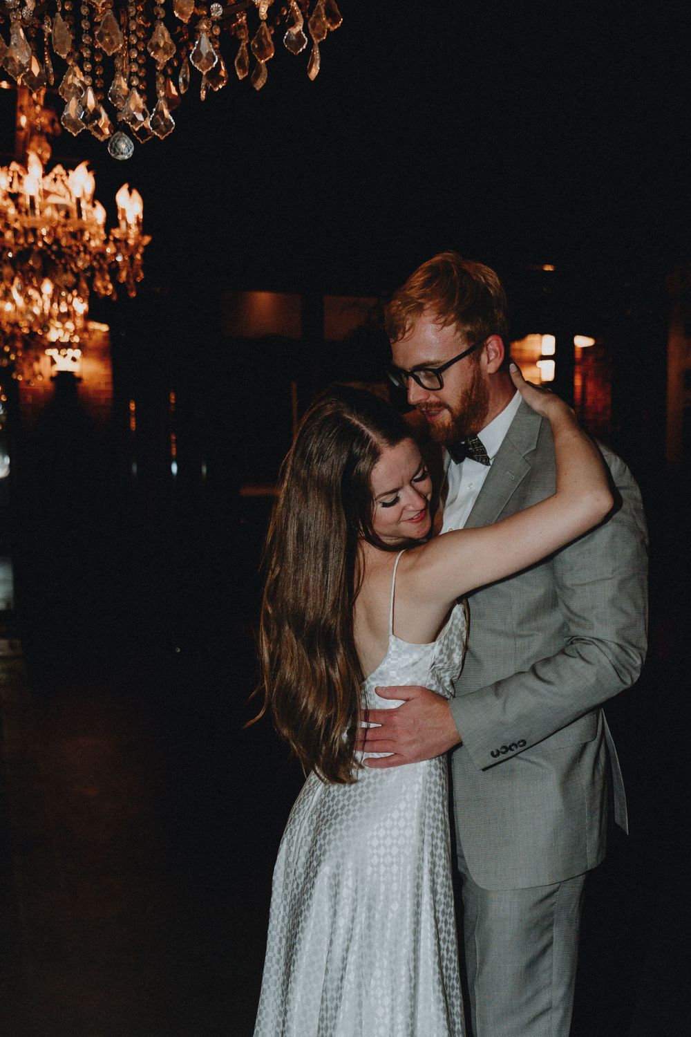 A couple dances with chandeliers behind them