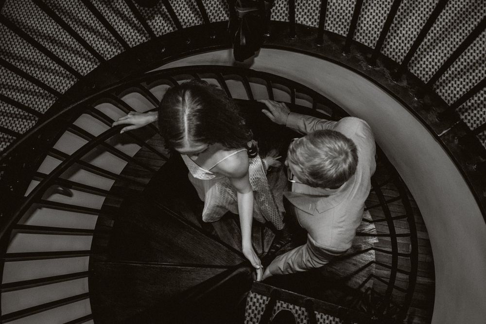 A black and white photo of a woman leading a man up a spiral staircase
