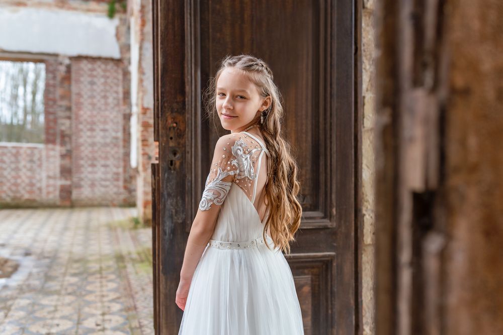 Elegant white lace dress captured in a rustic doorway setting with exposed brick walls.