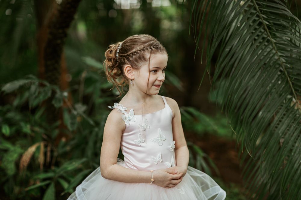 Young person wearing white formal dress smiles in tropical garden setting.