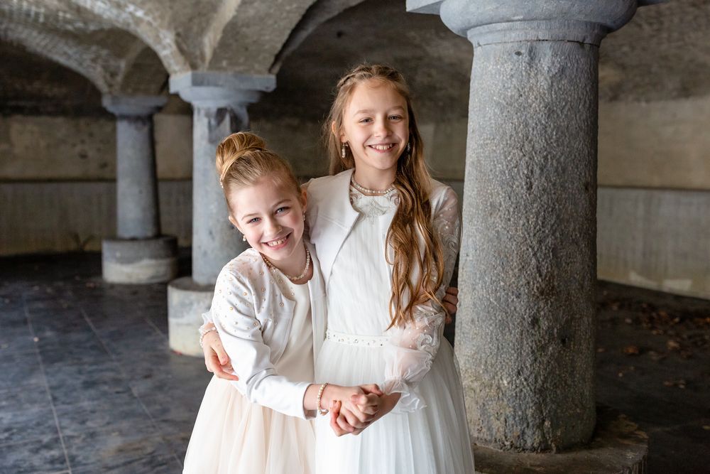 Two people sharing a joyful moment under stone archways in white dresses.