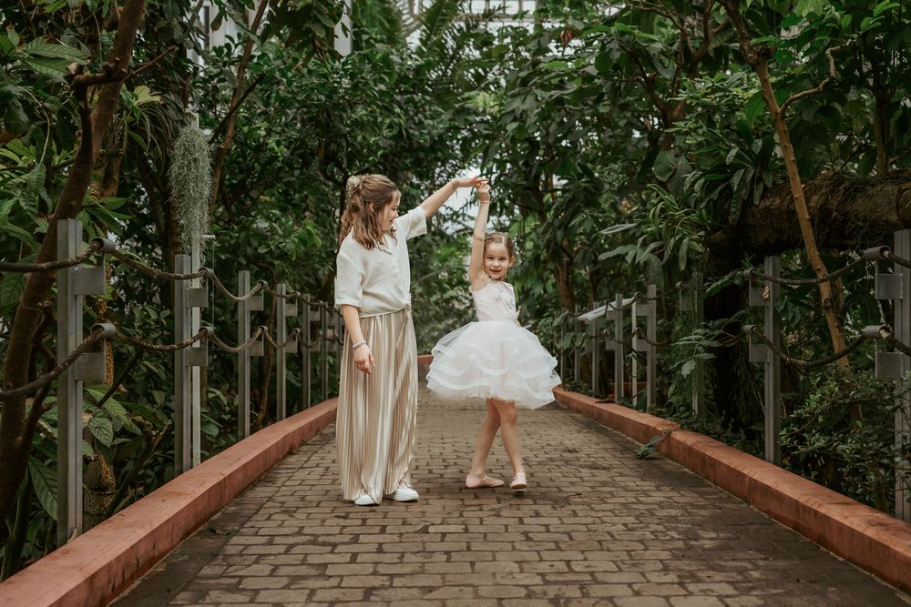 Two people in white outfits dancing together on a wooden bridge surrounded by greenery.