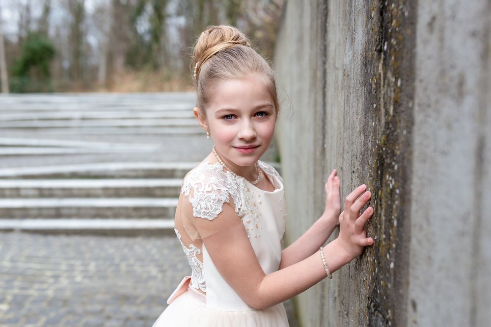 Sweet portrait against stone wall featuring white lace dress and elegant pose.