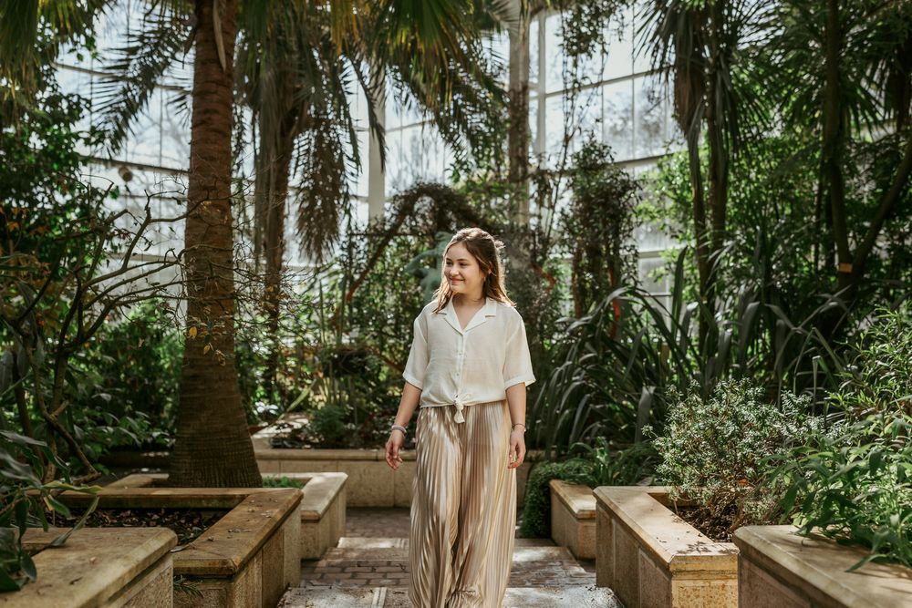 Someone in casual attire enjoying a moment in a lush greenhouse setting with wooden benches.