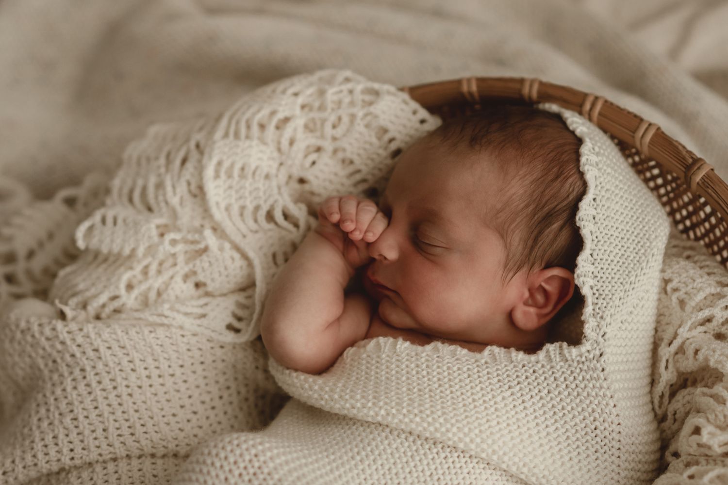 Newborn sleeping peacefully wrapped in cream knit blanket with delicate lace details.