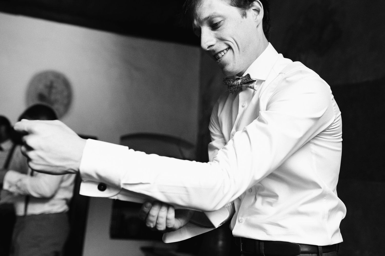 Black and white photo of a groom adjusting his formal attire.