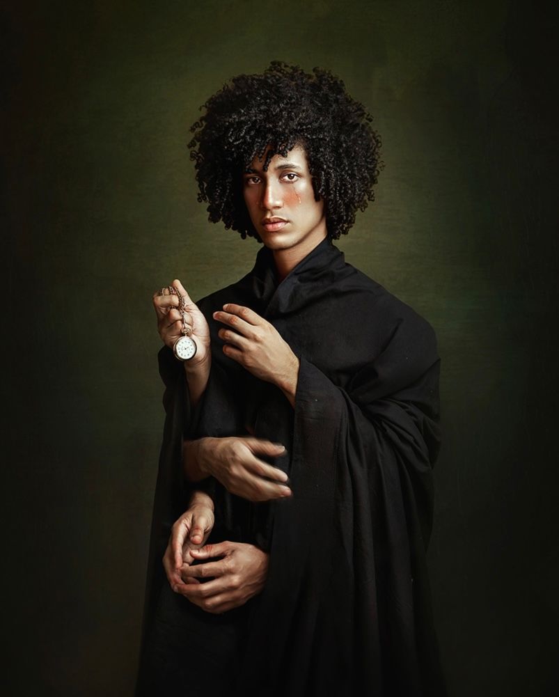 Dramatic portrait against dark background featuring black cloak and potion bottle.