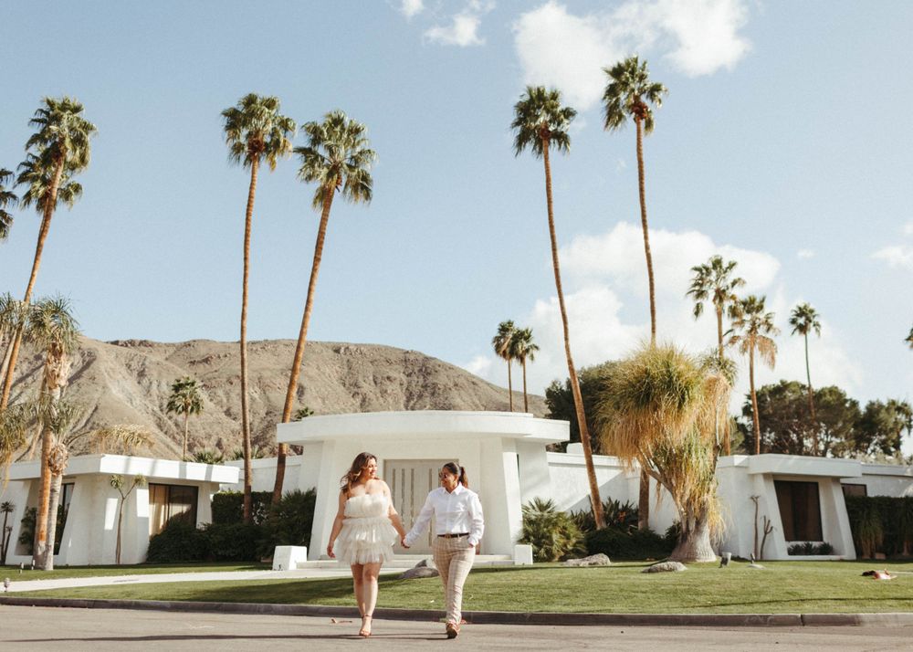 Two women walk holding hands, across the street in front of a Mid-Century Modern Home in Palm Springs