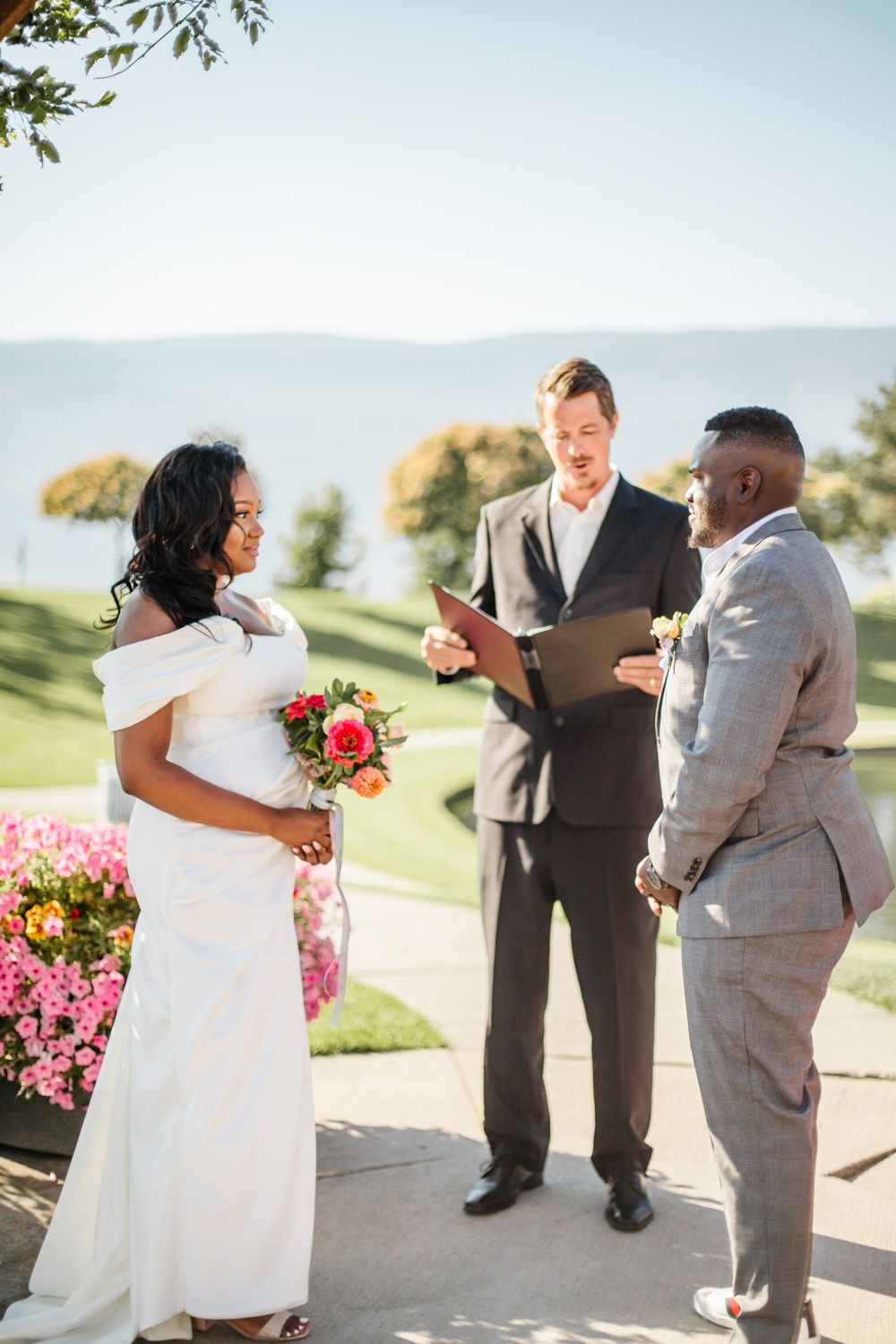 An intimate outdoor wedding ceremony takes place against a backdrop of mountains and pink flowers.