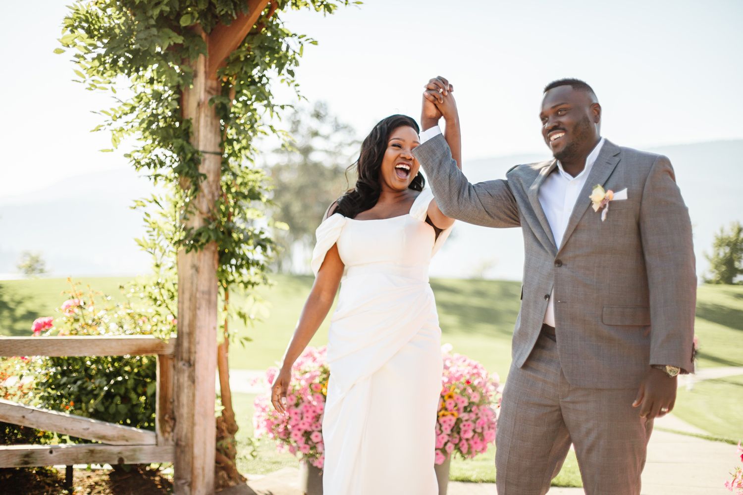 A couple celebrates their wedding day with laughter in a scenic outdoor setting.