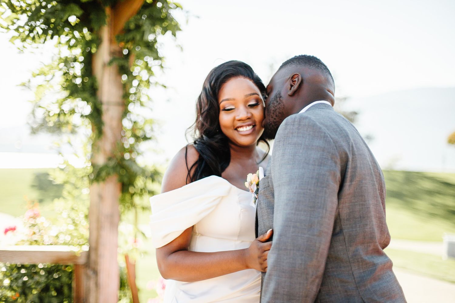 A couple shares an intimate moment outdoors in wedding attire with natural greenery surrounding them.