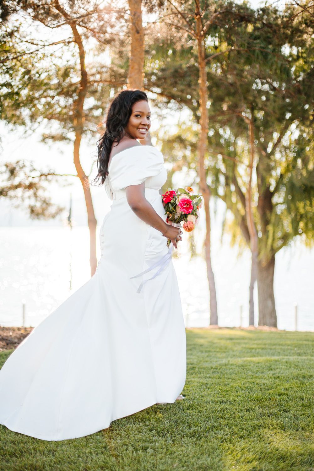 A bride in a flowing white dress twirls on a grassy hill during golden hour.