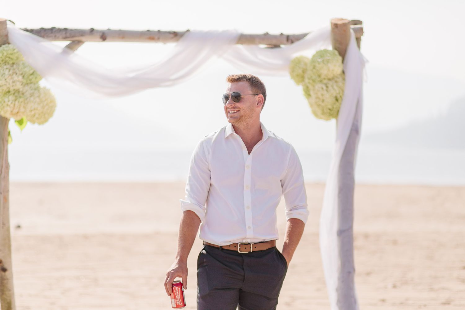Elegant beach wedding setup with white fabric draped arbor against a sandy backdrop.