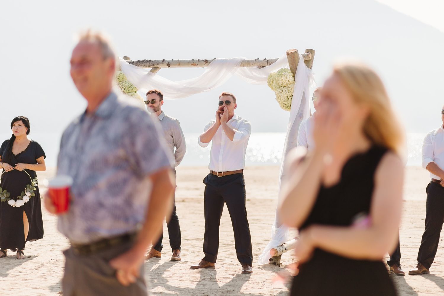 Wedding guests gathered on a sunny beach for an outdoor ceremony celebration.