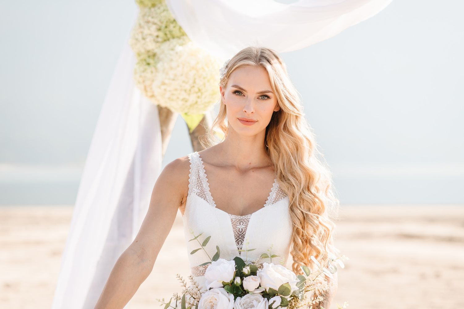 Elegant beach wedding dress with lace details and white bouquet.