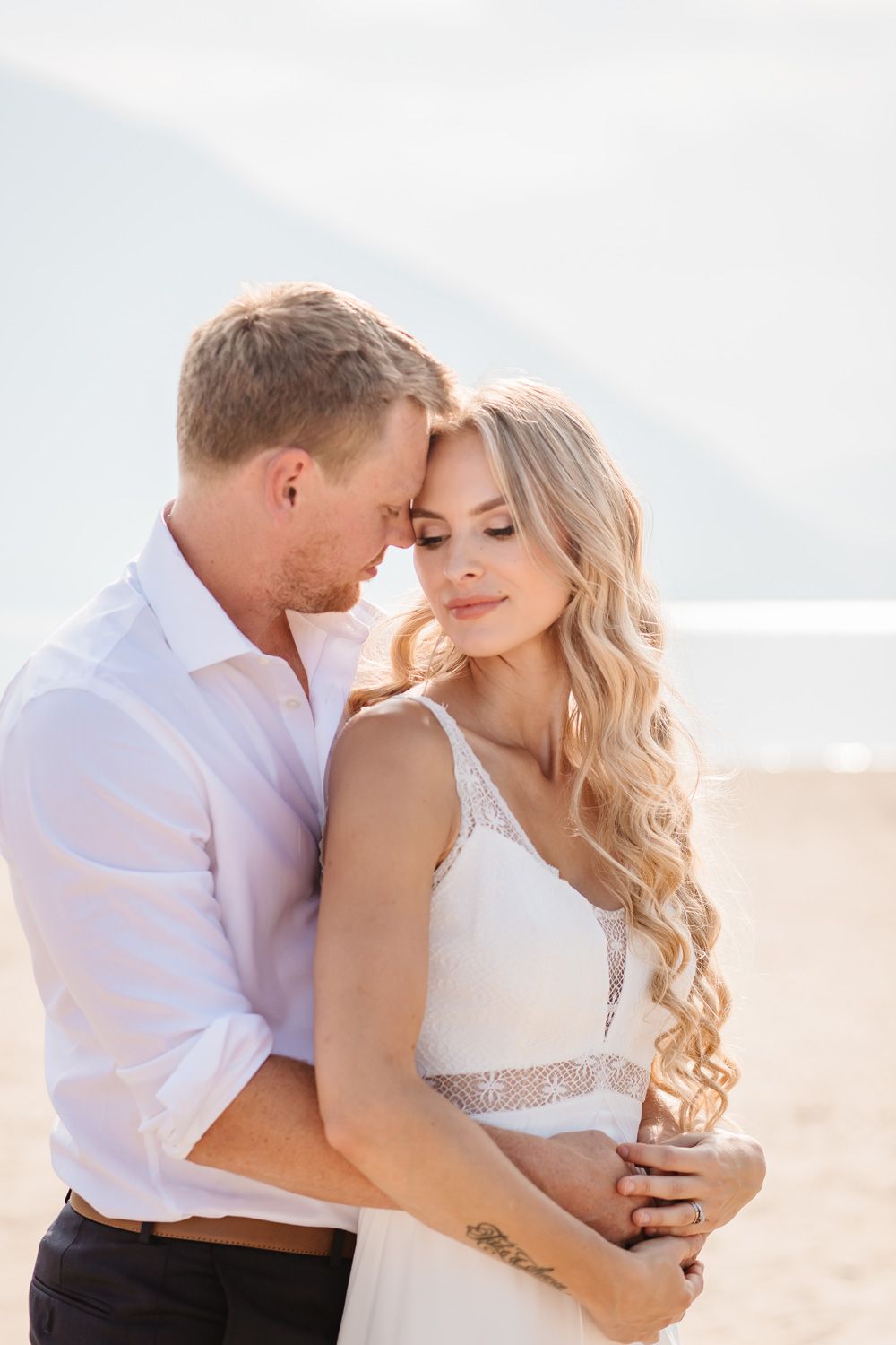 Romantic beach wedding photo shoot with couple embracing in soft natural light.