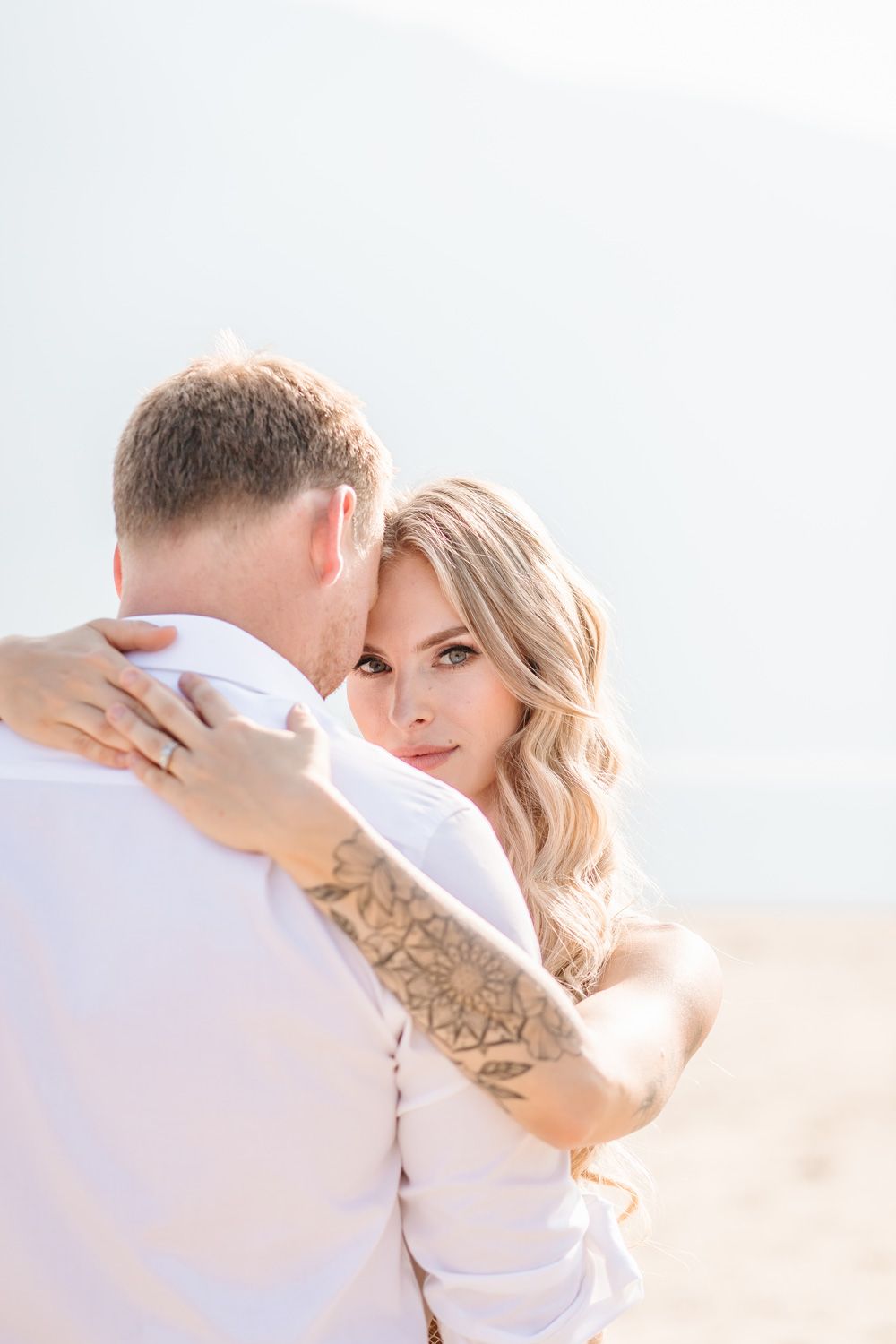 Intimate beach portraits of newlyweds sharing tender moments against bright background.