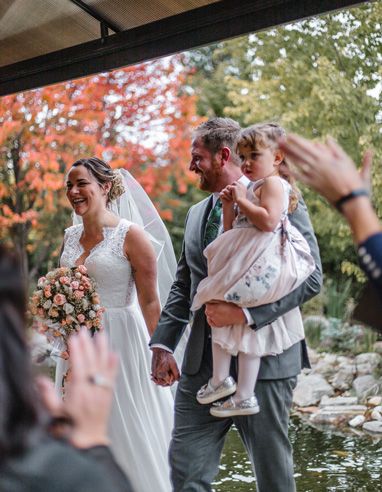 Wedding party gathered around water feature in autumn garden setting.