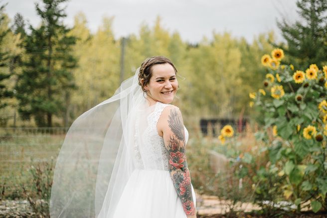 A bride in a white wedding dress and veil poses in front of sunflowers on her wedding day.
