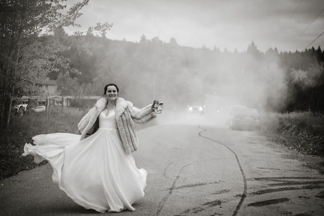 A bride in a flowing white dress and cardigan twirls on a misty road.