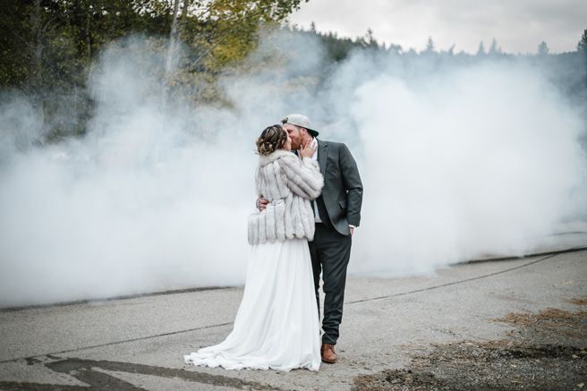A romantic wedding portrait surrounded by dramatic smoke effects on a paved road.