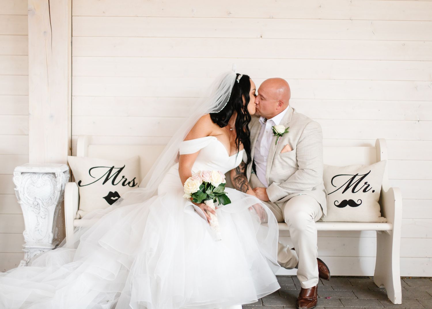 Wedding couple poses against white wall with Mr and Mrs signs.