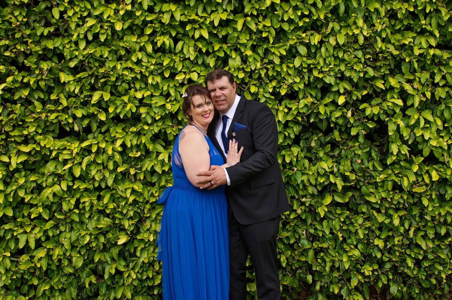 bride and groom posing infront of wall of green